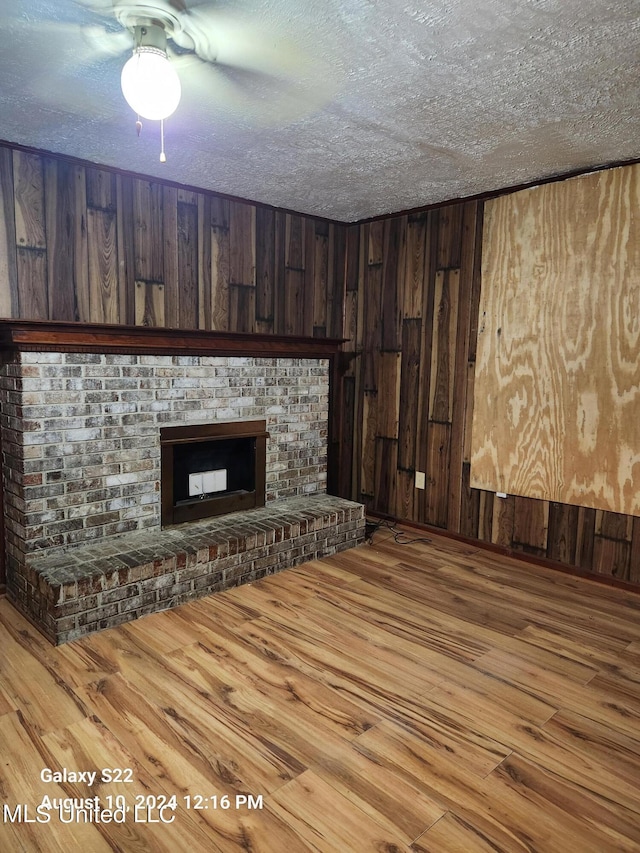 unfurnished living room with a textured ceiling, a fireplace, wood-type flooring, and wooden walls