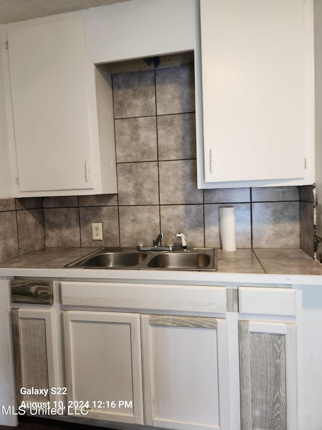 kitchen featuring decorative backsplash, white cabinets, and sink