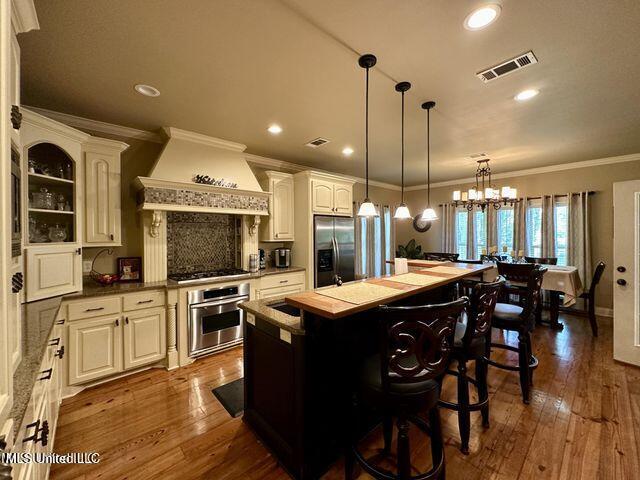 139 Glen Auburn Dr, Clinton, MS 39056 - kitchen with appliances with stainless steel finishes, crown molding, custom exhaust hood, hanging light fixtures, and dark wood-type flooring