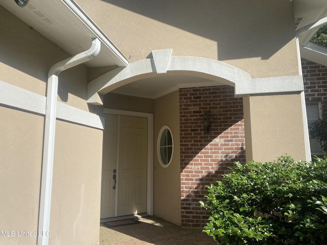 view of exterior entry with stucco siding and brick siding
