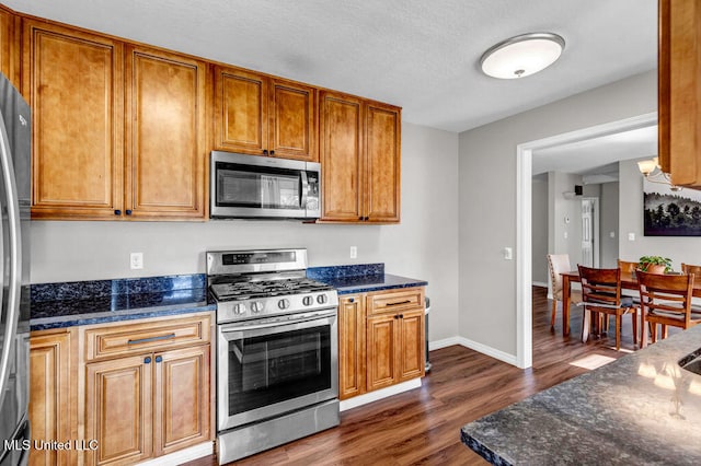 kitchen featuring appliances with stainless steel finishes, dark wood-style flooring, brown cabinets, and baseboards