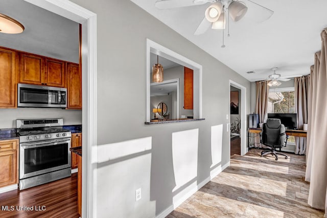 kitchen featuring dark countertops, appliances with stainless steel finishes, brown cabinetry, wood finished floors, and baseboards