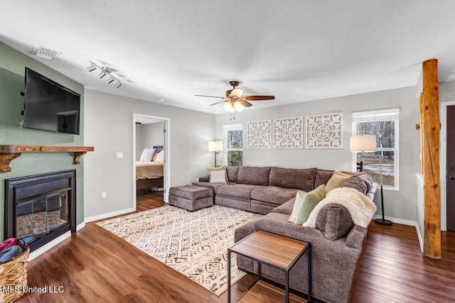 living area featuring wood finished floors, a glass covered fireplace, visible vents, and baseboards