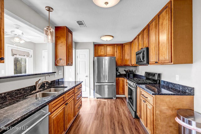 kitchen with wood finished floors, a sink, visible vents, appliances with stainless steel finishes, and brown cabinetry