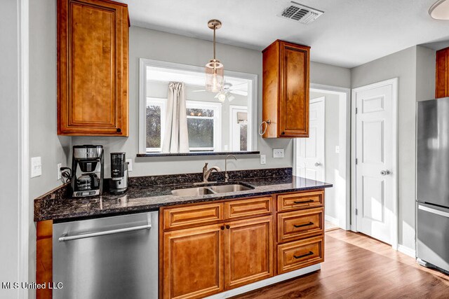 kitchen featuring stainless steel appliances, a sink, visible vents, dark stone countertops, and dark wood finished floors