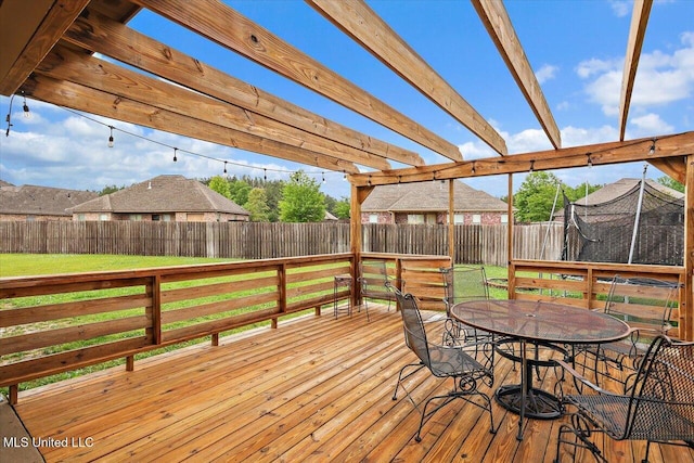 wooden terrace featuring a yard, outdoor dining area, a trampoline, and a fenced backyard