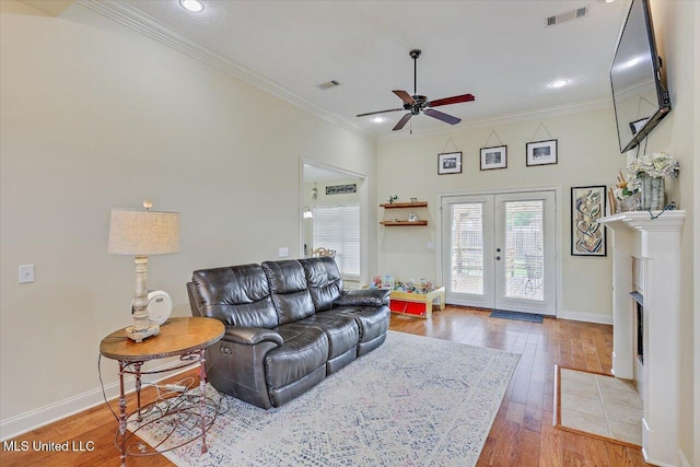 living room featuring crown molding, light wood-style flooring, visible vents, ceiling fan, and baseboards