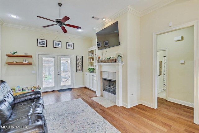 living room with a tiled fireplace, wood finished floors, ornamental molding, visible vents, and a ceiling fan