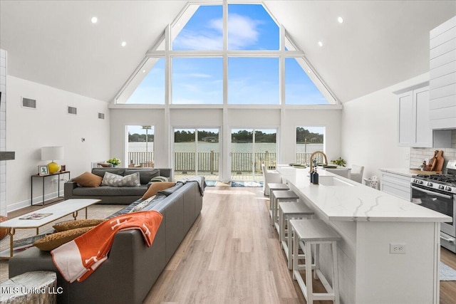 living room featuring sink, high vaulted ceiling, and light wood-type flooring