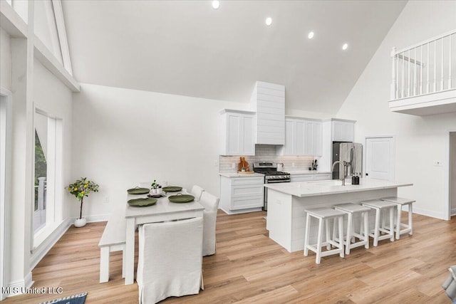 kitchen with high vaulted ceiling, an island with sink, white cabinets, a kitchen bar, and stainless steel appliances