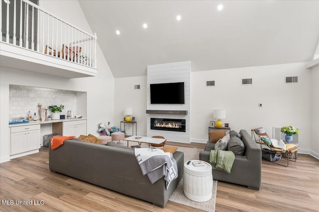 living room with a large fireplace, high vaulted ceiling, and light hardwood / wood-style flooring