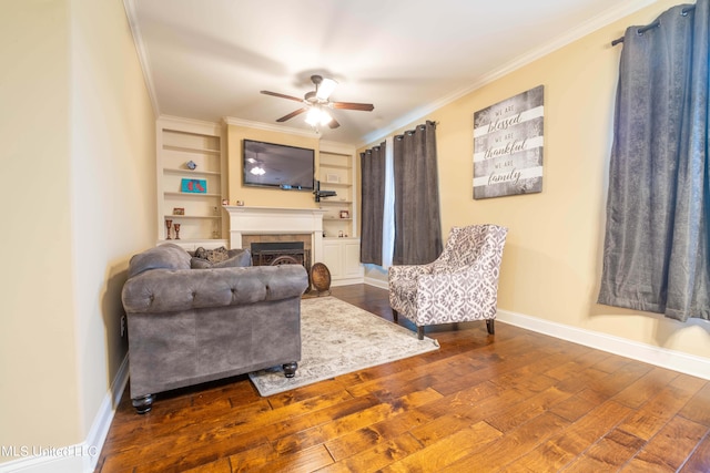 living room with a tiled fireplace, ceiling fan, dark hardwood / wood-style floors, built in shelves, and crown molding