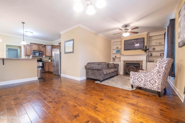 living room with ornamental molding, dark wood-type flooring, built in shelves, and ceiling fan