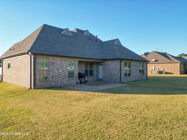 rear view of property featuring central AC unit, a patio area, a yard, brick siding, and roof with shingles