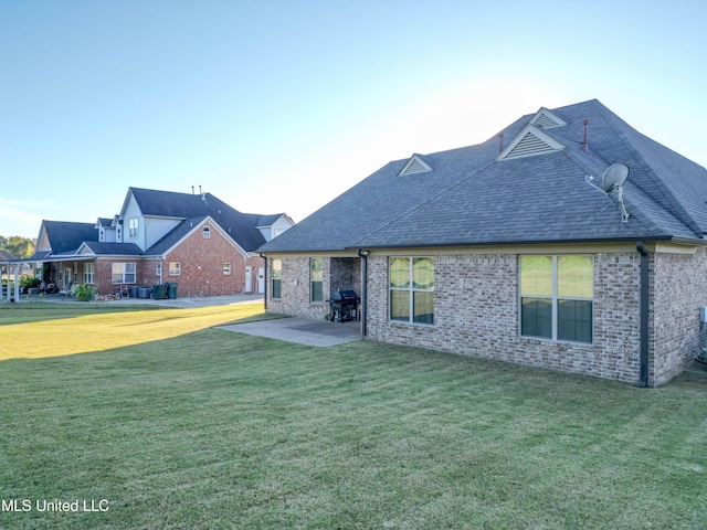 rear view of property featuring a patio, brick siding, roof with shingles, and a lawn