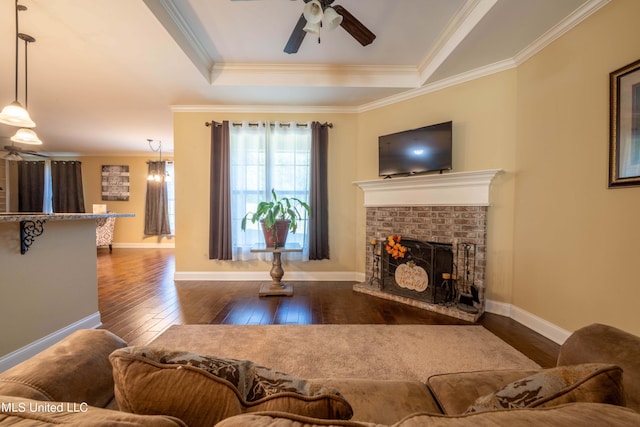 living area featuring hardwood / wood-style floors, ceiling fan, a fireplace, crown molding, and a tray ceiling