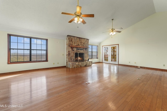 unfurnished living room with lofted ceiling, light hardwood / wood-style floors, a stone fireplace, and a healthy amount of sunlight