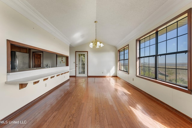 unfurnished living room featuring hardwood / wood-style floors, crown molding, vaulted ceiling, a textured ceiling, and a notable chandelier