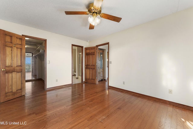 unfurnished bedroom featuring a walk in closet, a textured ceiling, ceiling fan, wood-type flooring, and a closet