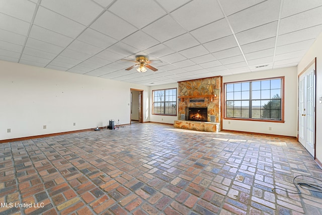 unfurnished living room featuring a paneled ceiling, ceiling fan, a fireplace, and a wealth of natural light