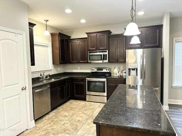 kitchen with hanging light fixtures, appliances with stainless steel finishes, a sink, dark brown cabinetry, and dark stone counters