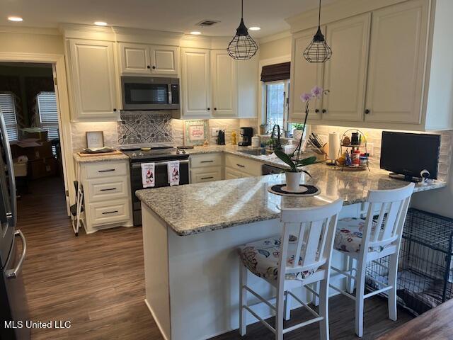 715 Sumner Ave, Greenwood, MS 38930 - kitchen featuring appliances with stainless steel finishes, white cabinetry, a peninsula, dark wood-type flooring, and a kitchen bar