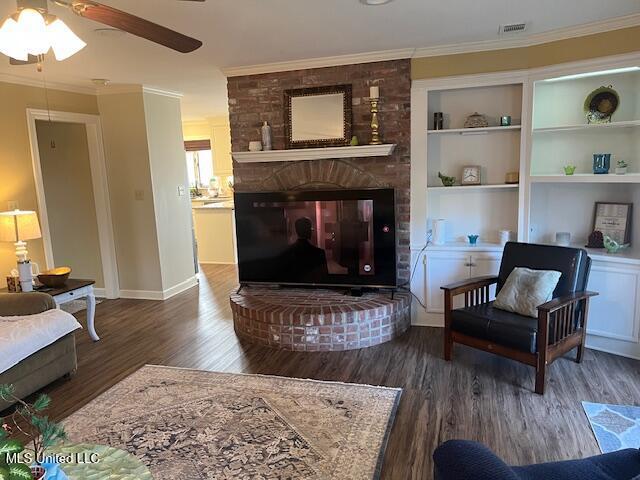 living room featuring ceiling fan, a fireplace, ornamental molding, and dark wood-type flooring