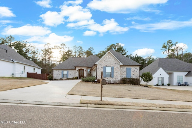 view of front of house with brick siding, driveway, roof with shingles, and fence