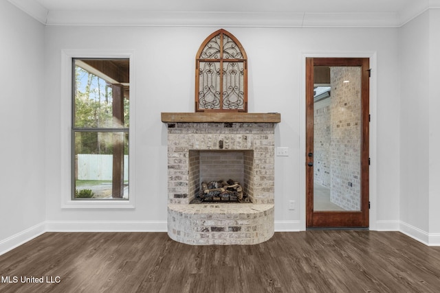 unfurnished living room with crown molding, a brick fireplace, dark wood-style floors, and baseboards