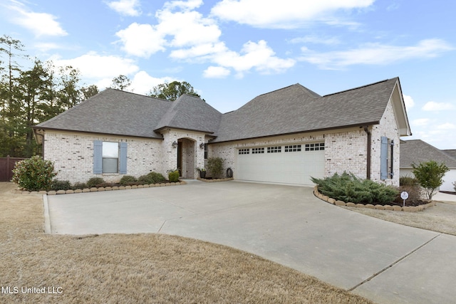 french country inspired facade featuring an attached garage, brick siding, driveway, and roof with shingles