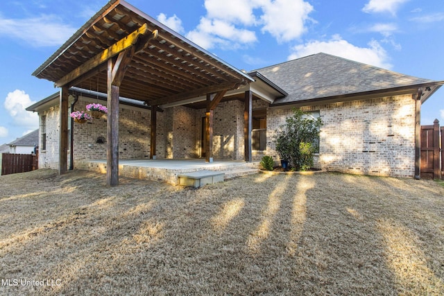 rear view of house with a patio area, brick siding, a shingled roof, and fence