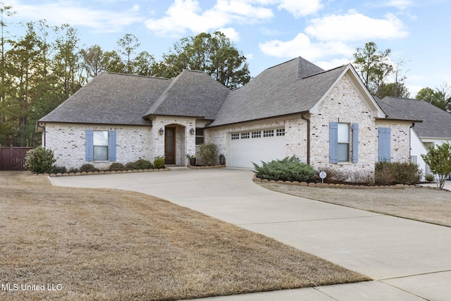 french country style house with brick siding, driveway, a garage, and roof with shingles