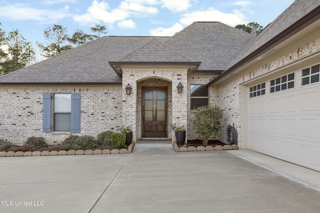 doorway to property featuring brick siding, concrete driveway, a shingled roof, and an attached garage