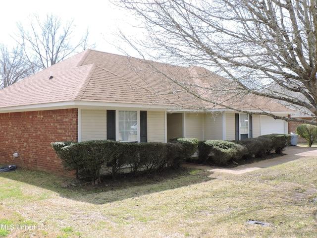 view of side of property featuring a garage, a yard, a shingled roof, and brick siding