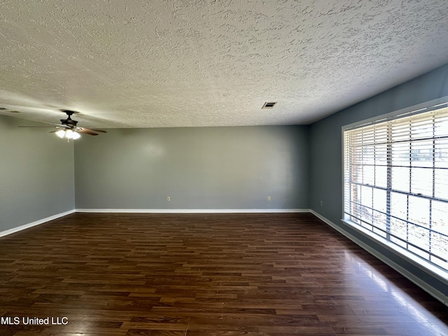 empty room featuring a textured ceiling, dark wood-type flooring, visible vents, and baseboards