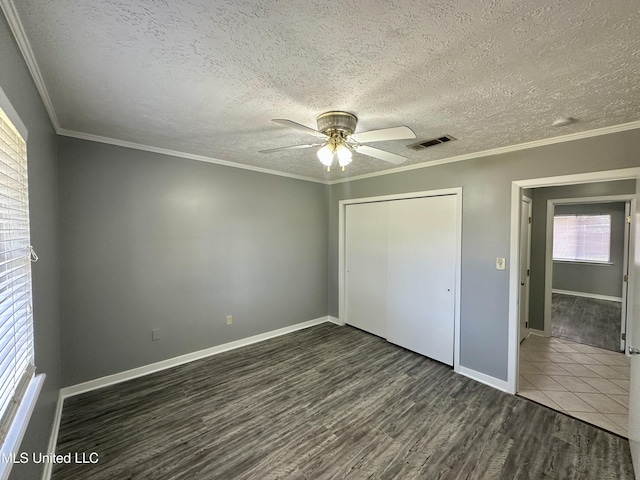 unfurnished bedroom with ornamental molding, a closet, wood finished floors, and visible vents