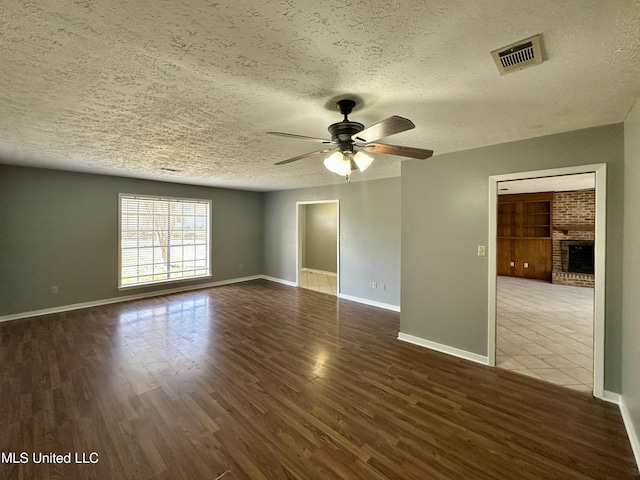 unfurnished room with visible vents, a ceiling fan, a brick fireplace, a textured ceiling, and wood finished floors