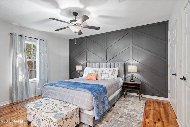 bedroom featuring wood finished floors, a ceiling fan, baseboards, and a decorative wall