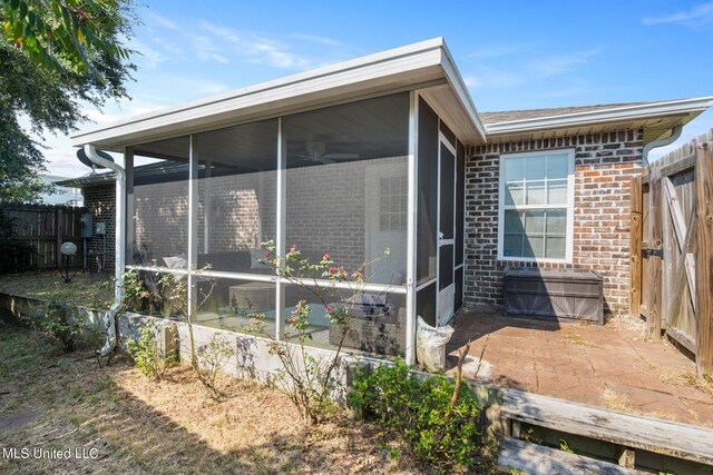 view of home's exterior with a sunroom, fence, brick siding, and a patio