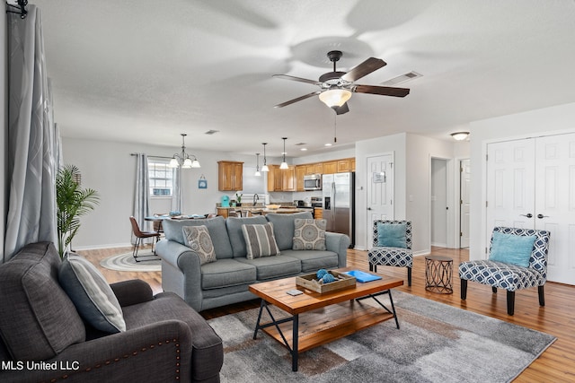 living room with visible vents, light wood finished floors, ceiling fan with notable chandelier, and baseboards