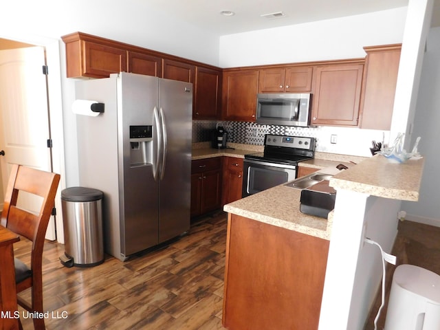 kitchen featuring a kitchen bar, kitchen peninsula, appliances with stainless steel finishes, dark hardwood / wood-style flooring, and sink