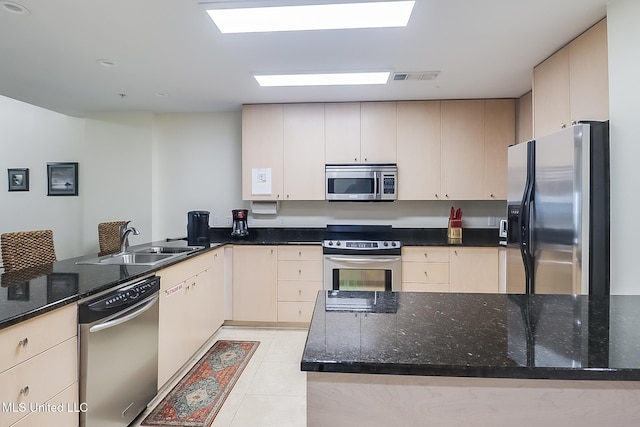 kitchen with light tile patterned floors, stainless steel appliances, dark stone countertops, and sink