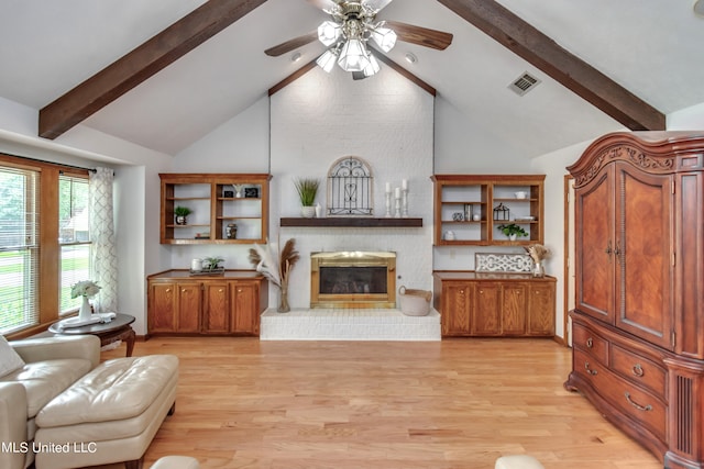 living room featuring ceiling fan, beamed ceiling, a brick fireplace, and light wood-type flooring