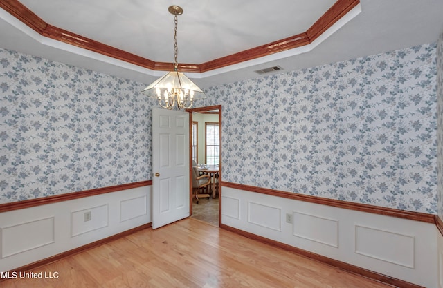 spare room with crown molding, a tray ceiling, a chandelier, and light wood-type flooring