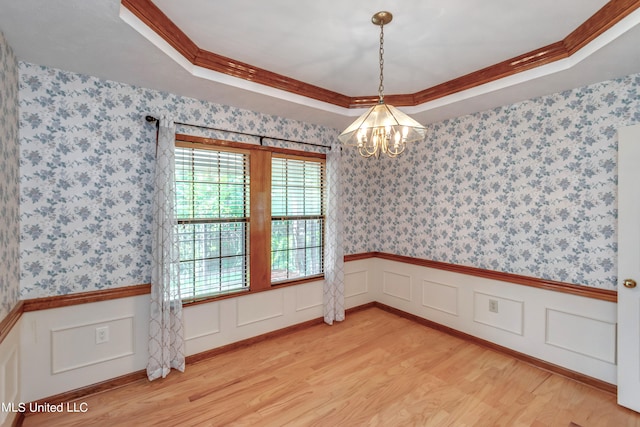 unfurnished room featuring a notable chandelier, ornamental molding, a raised ceiling, and light wood-type flooring