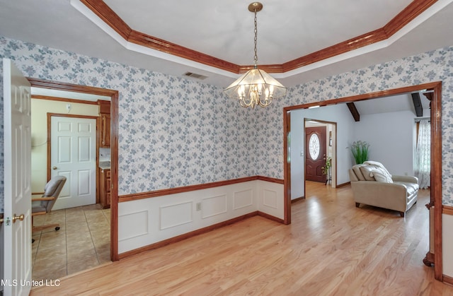 empty room featuring ornamental molding, an inviting chandelier, light hardwood / wood-style floors, and a tray ceiling