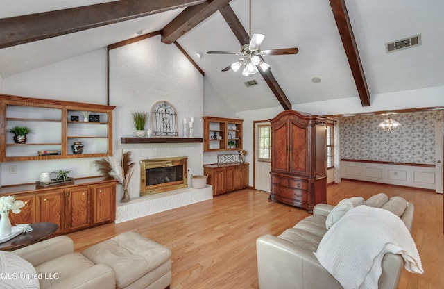 living room with ceiling fan, high vaulted ceiling, a brick fireplace, beamed ceiling, and light hardwood / wood-style floors