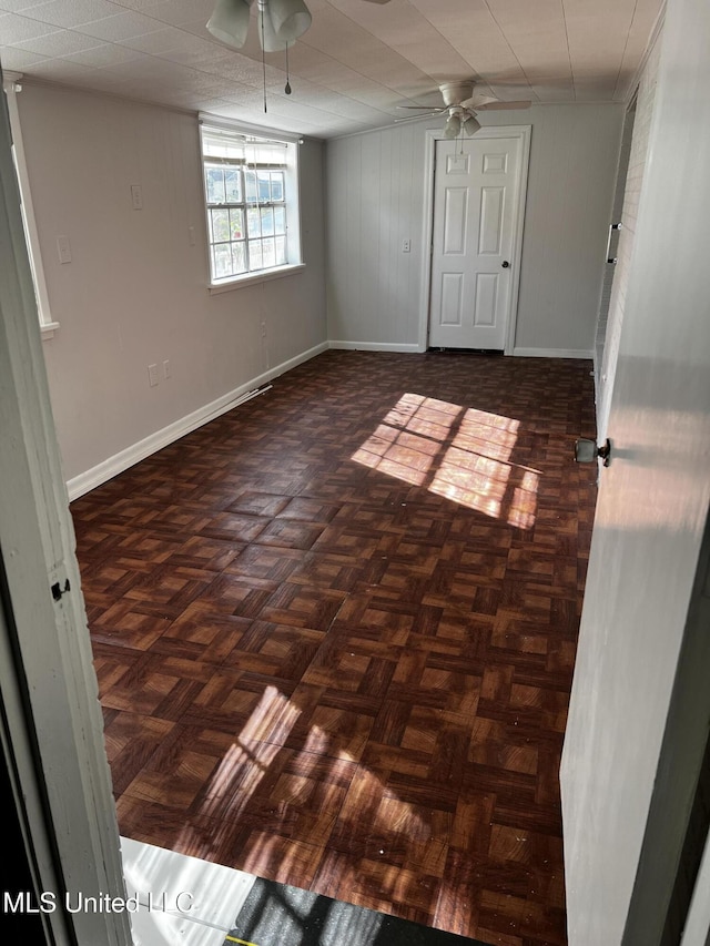 spare room with wood walls, ceiling fan, and dark parquet floors