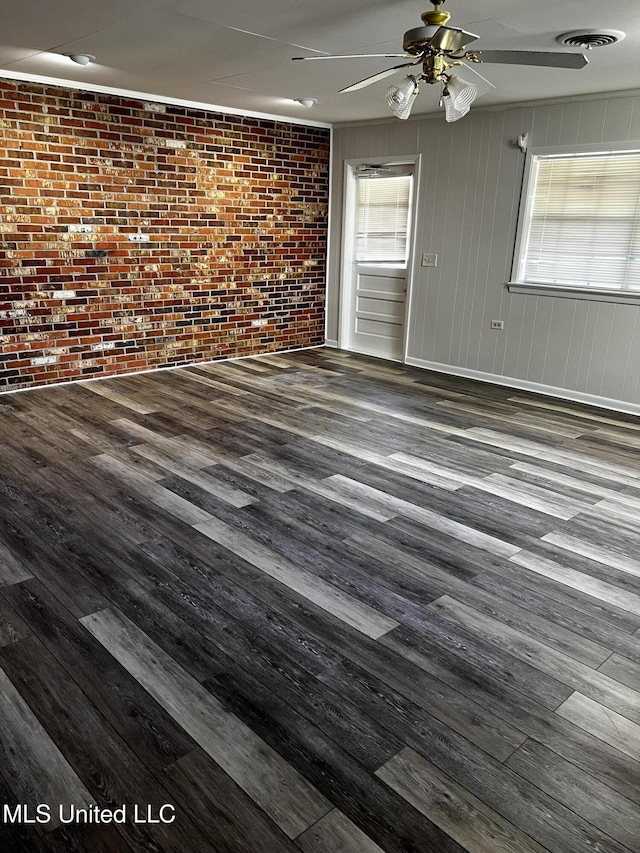 unfurnished room featuring brick wall, dark hardwood / wood-style floors, and a healthy amount of sunlight