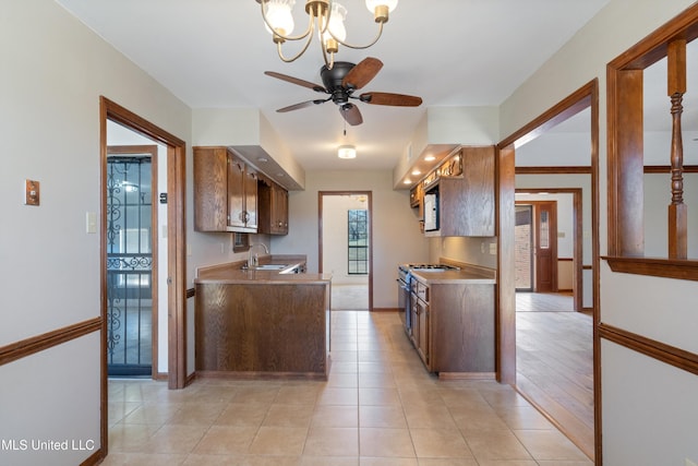 kitchen featuring light tile patterned floors, a sink, light countertops, stainless steel gas range oven, and ceiling fan with notable chandelier